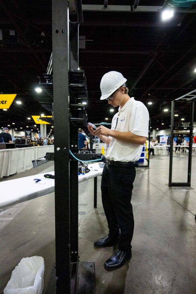 A technician in a hard hat inspects equipment at a trade show booth.
